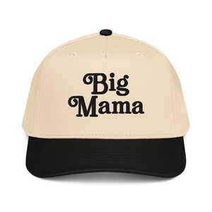 May include: A baseball cap with a cream-colored crown and a black brim. The words "Big Mama" are embroidered in a bold, black script across the front of the cap. The cap has a curved brim and a black button on top.