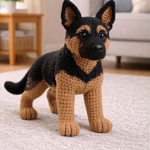 Op de afbeelding: Een gehaakte Duitse herder hond figuur in zwart en bruin. Het handgemaakte pluche dier heeft een zwarte kop, rug en staart, met bruine poten, borst en gezicht. De hond staat op een lichtgekleurd tapijt.