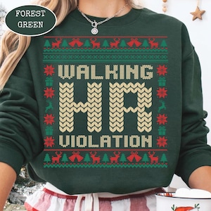 May include: Forest green sweatshirt with the text "WALKING HR VIOLATION" in a knitted style. The sweatshirt has a festive pattern of reindeer, Christmas trees, and bells in red and green. A white mug with a Santa Claus graphic is visible.