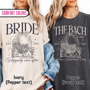 May include: Two t-shirts, one ivory and one pepper, with graphic text. The ivory shirt says "BRIDE" above a globe design and "Happily ever after." The pepper shirt says "THE BACH Club" with "Victoria's Bachelorette Party."