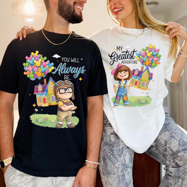 K&ouml;nnte beinhalten: Schwarze und wei&szlig;e T-Shirts mit Cartoon-Grafiken. Das schwarze Shirt zeigt eine Figur mit Brille, ein Haus und den Text "You Will Always Be...". Das wei&szlig;e Shirt zeigt ein M&auml;dchen, ein Haus und den Text "My Greatest Adventure".