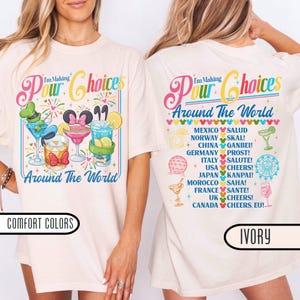 May include: An ivory t-shirt featuring a colorful graphic print. The front displays cocktails and the text I'm Making Pour Choices Around The World. The back lists countries and international toasts with small icons and colorful mouse-ear accents.