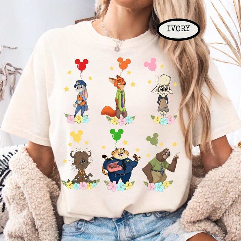K&ouml;nnte beinhalten: Elfenbeinfarbenes T-Shirt mit Cartoon-Charakteren aus Zootopia, die jeweils einen Ballon halten. Die Charaktere sind von Blumen und Sternen umgeben. Das Wort "IVORY" ist oben rechts auf dem Shirt aufgedruckt.