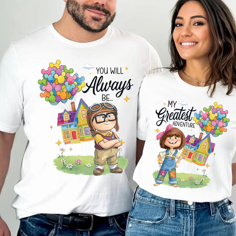 K&ouml;nnte beinhalten: Wei&szlig;e T-Shirts mit passenden Cartoon-Grafiken. Ein Shirt zeigt einen Jungen mit Brille und dem Text "You Will Always Be..". Das andere Shirt hat ein M&auml;dchen und den Text "My Greatest Adventure". Beide Shirts haben bunte Ballongruppen.
