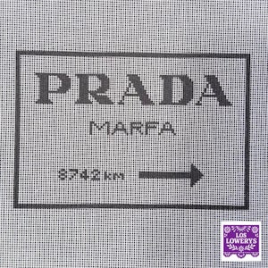 May include: A gray canvas with a black rectangular border featuring the text "PRADA MARFA" above "8742km" and an arrow. The lower right corner has a small logo with the text "LOS LOWERY'S".