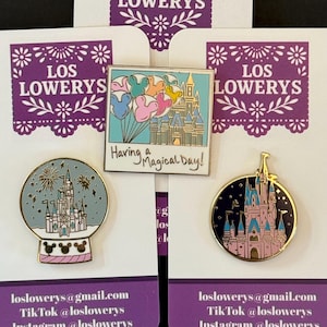 Op de afbeelding: Drie emaille pins met Disney kasteelontwerpen. Eén pin toont een kasteel in een sneeuwbol, een andere heeft een kasteel met Mickey Mouse ballonnen, en de derde heeft een kasteel tegen een donkerblauwe achtergrond. De tekst "Having a Magical Day!" staat op één pin.