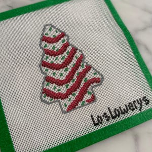 May include: A Christmas tree needlepoint design with red and green accents on a white background. The tree has red wavy stripes and green dots. The design is framed by a green border and includes the text "LosLowerys".