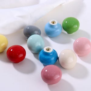 May include: A selection of colourful ceramic cabinet knobs in shades of red, blue, green, pink, and yellow. Each knob is round with a glossy finish and a metal threaded insert. Perfect for furniture upgrades and DIY projects.