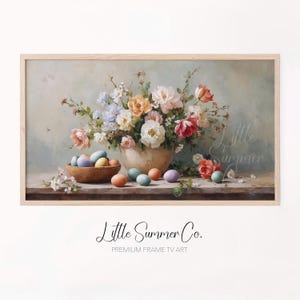Può includere: Stampa incorniciata con una natura morta di fiori e uova di Pasqua. Un vaso trabocca di fiori rosa, bianchi, arancioni e blu. Una ciotola di legno contiene uova colorate. Il testo "Little Summer Co." è in basso.
