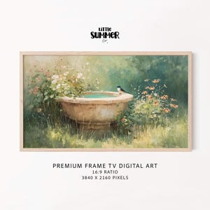 May include: A framed digital art print depicts a serene garden scene. A stone bird bath is surrounded by lush greenery and flowers. A small bird perches on the edge of the bath. The artwork is labeled "Little Summer Co." and "Premium Frame TV Digital Art."