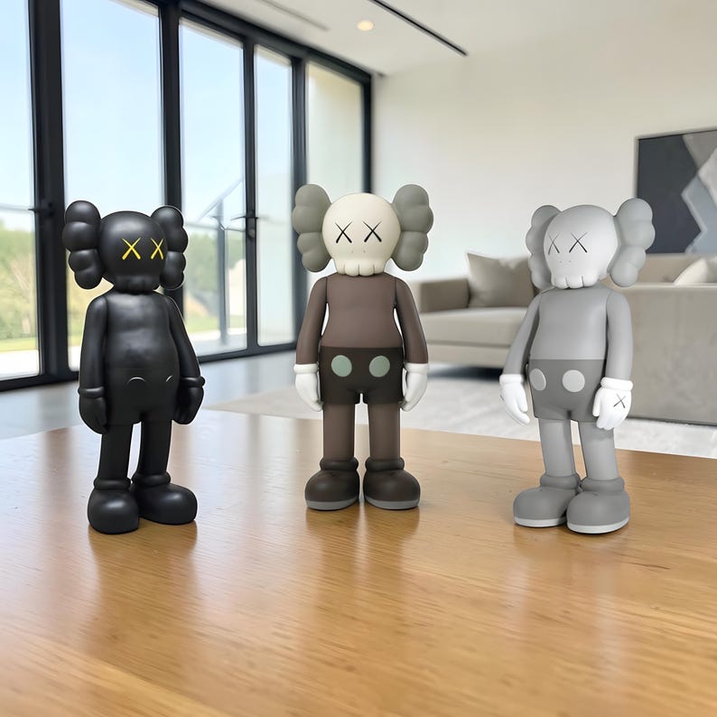 May include: Three collectible vinyl figures in black, brown, and gray, each with distinctive X-shaped eyes and a rounded head. The figures stand on a wooden surface, showcasing a modern art aesthetic. The figures have white gloves and shorts with two circles.