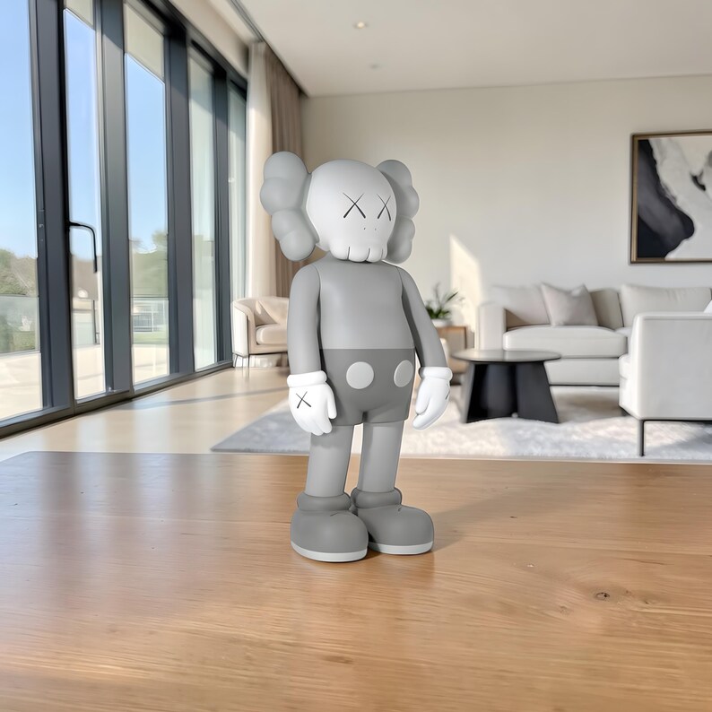 May include: A gray vinyl figure with a skull-like head and crossed-out eyes. The figure has gray shorts, gloves with an X on each hand, and large gray shoes. The figure is standing on a wooden surface in a well-lit room.