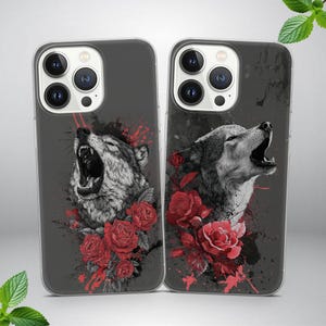 May include: Two phone cases with a wolf design. The cases feature a gray background with a detailed illustration of a howling wolf, red roses, and a splatter effect. The cases are designed for a smartphone.