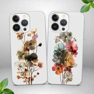 Puede incluir: Dos fundas transparentes para teléfono con diseños florales. Una funda presenta flores secas en tonos marrón, crema y verde. La otra funda muestra un colorido arreglo de flores rosas, azules y amarillas. Ambas fundas tienen un diseño transparente y protector.