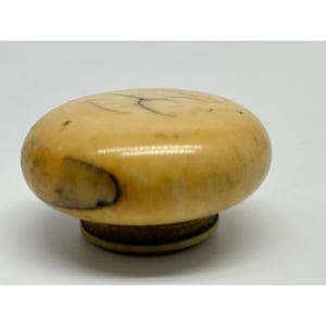 May include: A vintage, oval-shaped knob with a light tan color and dark brown veining. The knob has a circular base and a smooth, rounded top. The overall design suggests a classic or antique aesthetic.