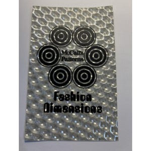 May include: A rectangular silver metallic sheet with a raised honeycomb texture. The center features a black circular logo with the text McCall's Patterns, surrounded by six black concentric circles. Below, the text Fashion Dimensions is printed.