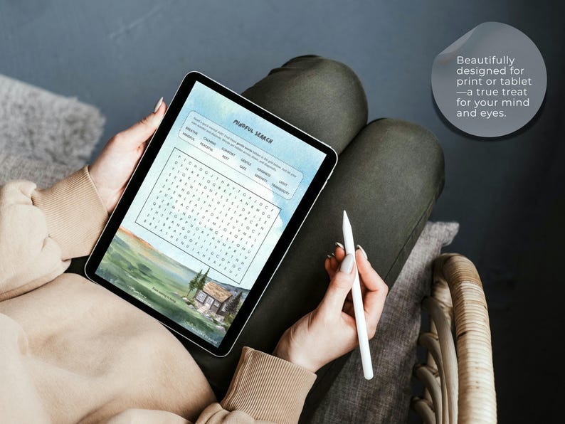 Op de afbeelding: Een tablet met een digitale woordzoeker genaamd Mindful Search en een landschapsillustratie van een huis in een veld. Het scherm bevat een tekstballon met de tekst: Beautifully designed for print or tablet&mdash;a true treat for your mind and eyes.