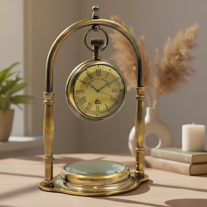 May include: A brass-colored desk clock with a vintage design. The clock face is gold with Roman numerals and a small logo. The clock is suspended within an arched frame, with a magnifying glass at the base. The clock is approximately 8 inches tall.