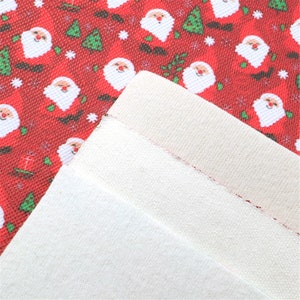 May include: Red fabric with a repeating pattern of Santa Claus and Christmas trees. The fabric is folded over to show the white underside.