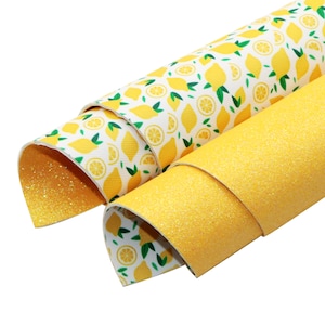 May include: Two rolls of yellow glitter fabric with a lemon print. One roll is solid yellow glitter and the other has a white background with yellow lemons and green leaves.