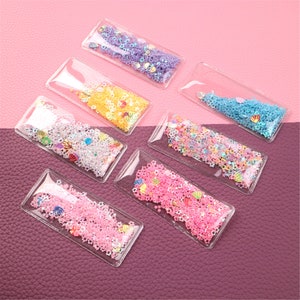 May include: Eight clear plastic hair clips with different colored glitter and sequins inside. The clips are rectangular and have a silver metal clasp.
