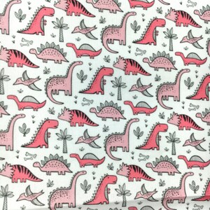 May include: A white fabric with a pink and gray dinosaur pattern. The dinosaurs are in various poses, including walking, running, and standing. There are also small gray bones and leaves scattered throughout the fabric.