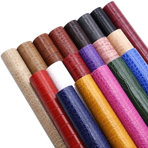 May include: Assortment of faux leather rolls in various colors, including red, blue, green, yellow, brown, and white. The rolls have a crocodile embossed pattern.