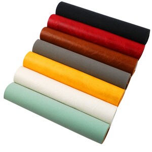 May include: A set of eight faux leather sheets in various colours, including black, red, brown, grey, yellow, white, and green. The sheets are rolled up and stacked on top of each other.