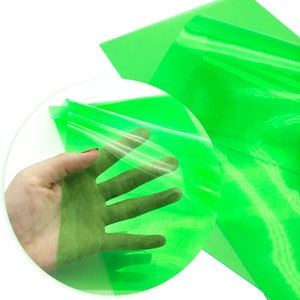 May include: A sheet of bright green translucent vinyl, folded in half and held in a hand. The vinyl is smooth and shiny, and it is clear enough to see through.