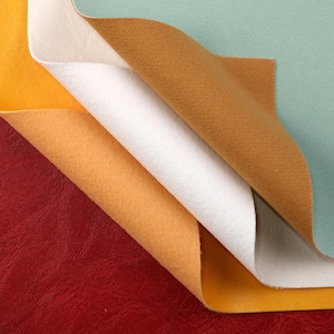 May include: Close-up of four fabric swatches in different colours: red, orange, yellow, and white. The swatches are folded over each other, creating a layered effect.