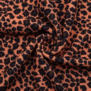 May include: Close-up of a peach-colored fabric with a black leopard print. The fabric has a textured, waffle-like surface.