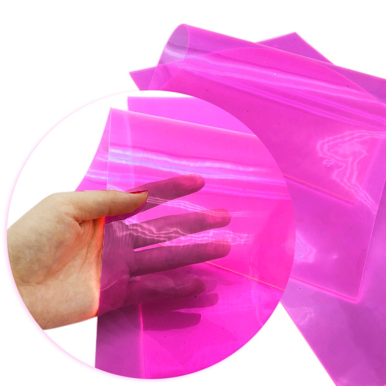 May include: A sheet of translucent pink iridescent vinyl. The vinyl is folded in half and a hand is holding the sheet up.