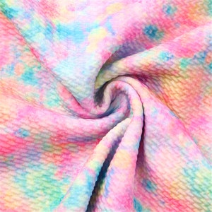 May include: A close-up of a pink, blue, and yellow tie-dye fabric with a textured waffle weave.