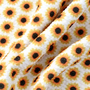 May include: White fabric with a repeating pattern of yellow sunflowers with black centers.