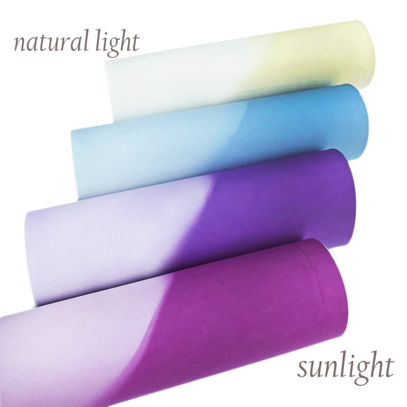 May include: Four rolls of paper in shades of blue, purple, and white, with a gradient effect. The text "natural light" and "sunlight" are visible. The rolls are arranged diagonally, showcasing the color transitions.