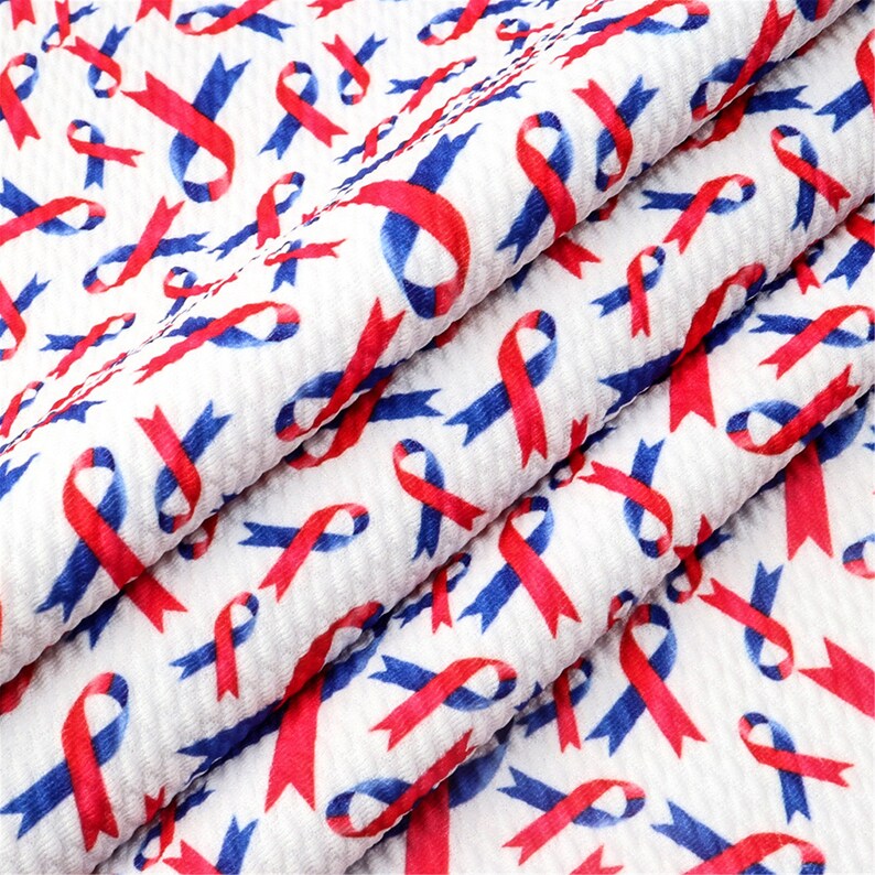 May include: White fabric with a repeating pattern of red and blue ribbon designs. The fabric is folded and textured.