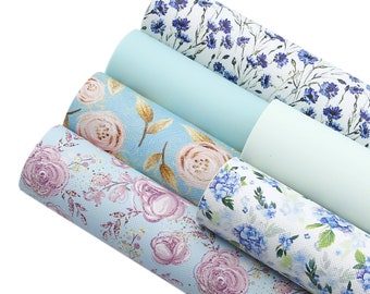 May include: Five rolls of blue and white floral patterned faux leather. The patterns include blue flowers on a white background, pink roses on a light blue background, blue hydrangeas on a white background, and a light blue background with pink roses and gold leaves.