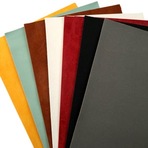 May include: A collection of seven different coloured leather swatches. The swatches are arranged in a fan shape, with the yellow swatch at the bottom and the grey swatch at the top. The swatches are all smooth and have a slight sheen.