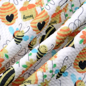 May include: White fabric with a repeating pattern of bees, honeycombs, and the word "honey".