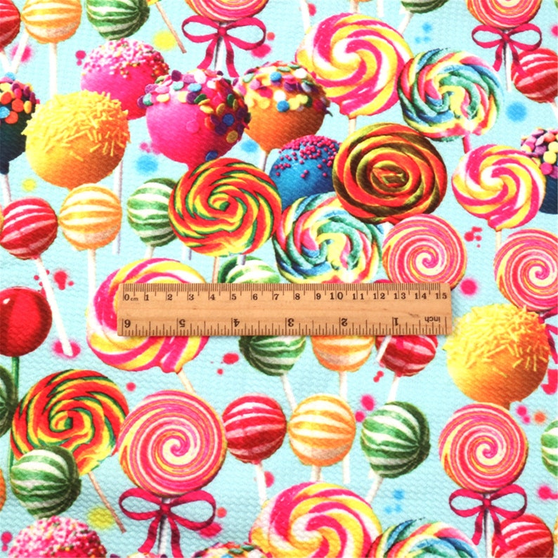 May include: A blue fabric with a repeating pattern of colorful lollipops and cake pops on sticks. The fabric is textured and has a slight sheen.