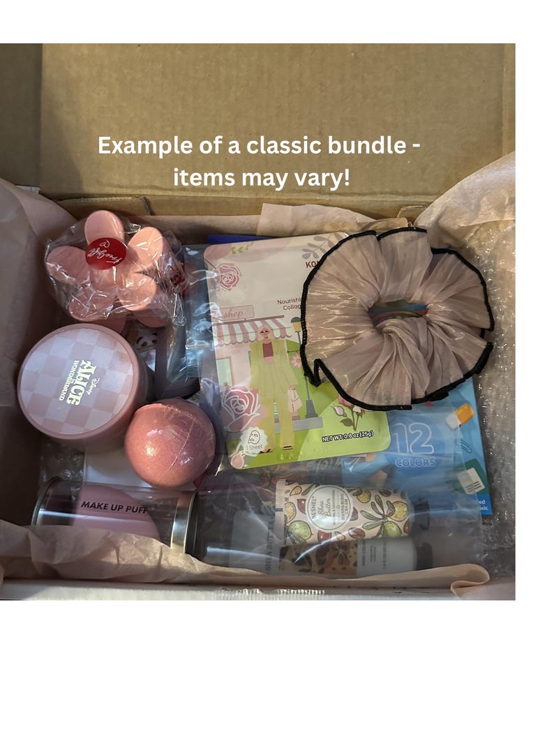 May include: A box filled with beauty products, including a pink flower-shaped container, a round pink compact, a pink bath bomb, and a scrunchie. The box also contains a tube of lotion, a face mask, and a makeup puff. Text on the box reads "Example of a classic bundle - items may vary!"