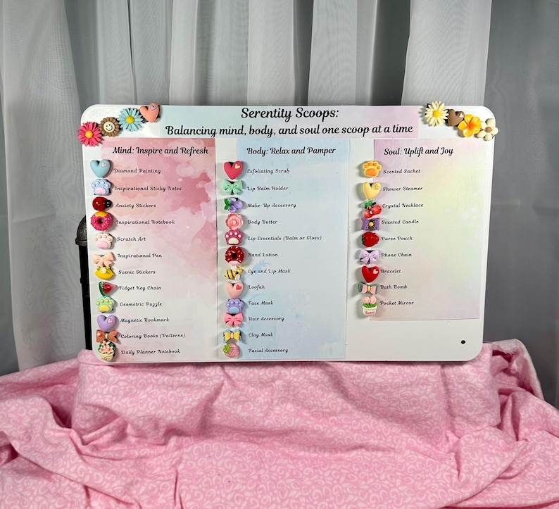 May include: A white rectangular sign with the text "Serenity Scoops" and product categories: Mind, Body, and Soul. The sign is decorated with colorful heart and flower-shaped embellishments. The categories list items like "Diamond Painting" and "Exfoliating Scrub".