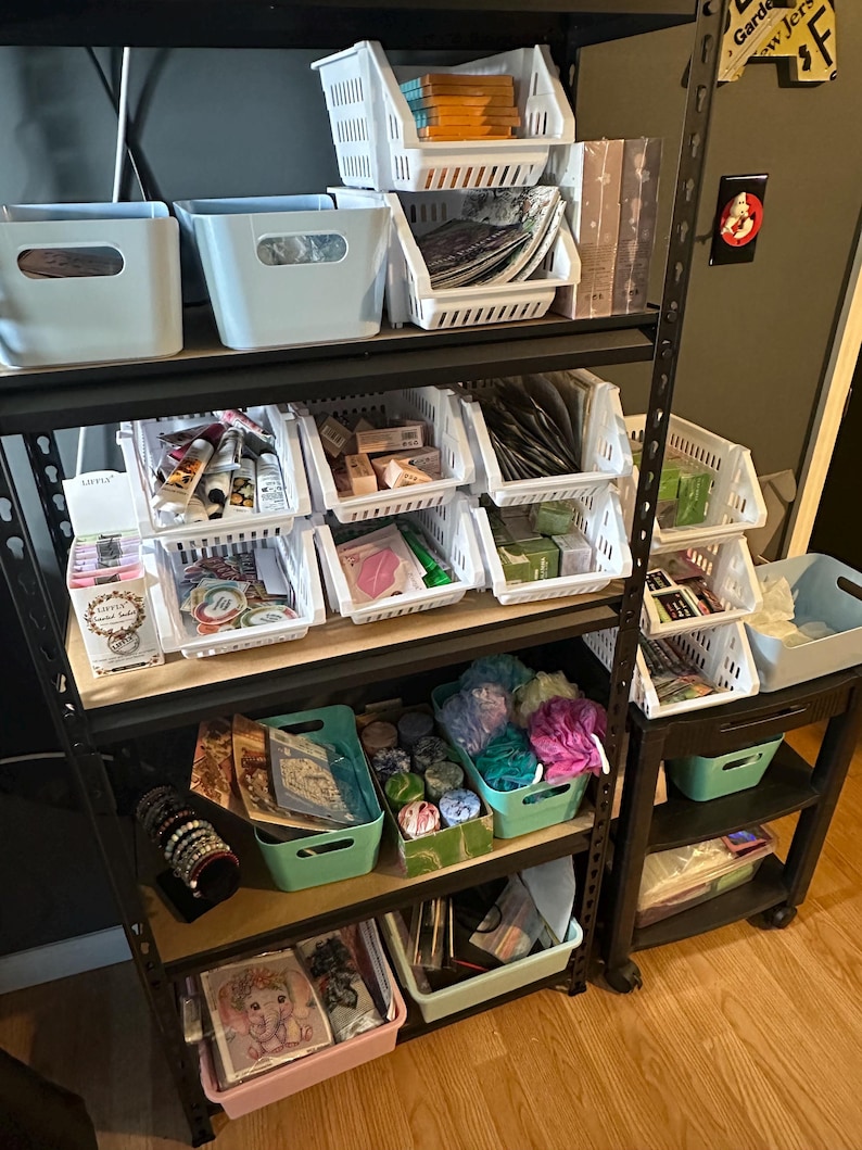 May include: A multi-tiered storage rack filled with various items. The top shelves hold light blue bins and white plastic baskets. The lower shelves contain more bins and baskets with a variety of products, including jewelry, bath products, and stationery.