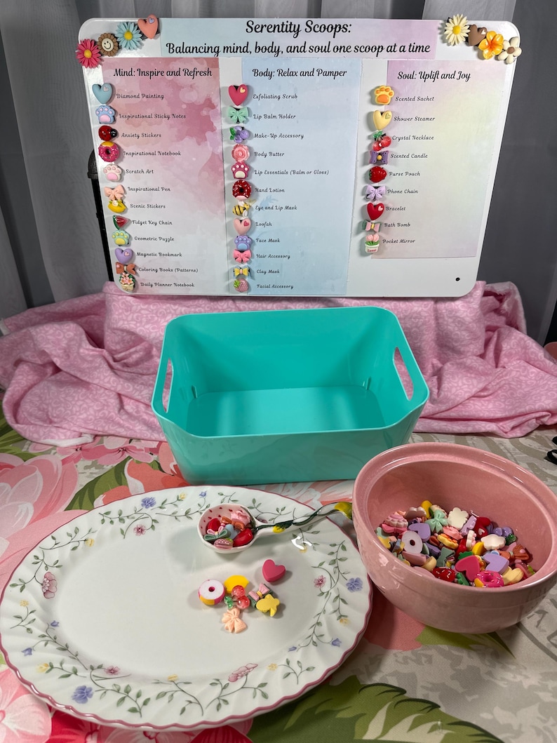 May include: A display featuring a sign with the text "Serenity Scoops" and product categories. A teal bin, a pink bowl, and a floral plate with a spoon are in the foreground. The plate and spoon hold colorful, decorative embellishments.