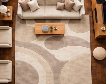 May include: Overhead view of a living room with a beige sofa, matching pillows, and a wooden coffee table. A large area rug with a circular pattern in shades of beige and brown covers the floor. Two armchairs and a side table are also visible.