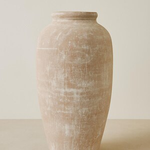 May include: A tall, beige-colored vase with a textured surface. The vase has a wide base that tapers upwards to a narrower neck and a rounded rim. The neutral color and simple design make it suitable for various decor styles.