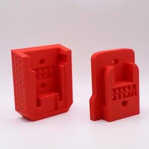 May include: Two bright red, 3D-printed plastic components. One has a textured honeycomb pattern on its side. Both have rectangular and circular openings. The components appear to be designed to fit together.