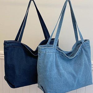 May include: Two denim tote bags hanging from metal hooks. One bag is a dark indigo color, and the other is a lighter blue wash. Both bags have long, thin straps and a rectangular shape. The text "XZminimalistBag" is visible in the bottom right corner.