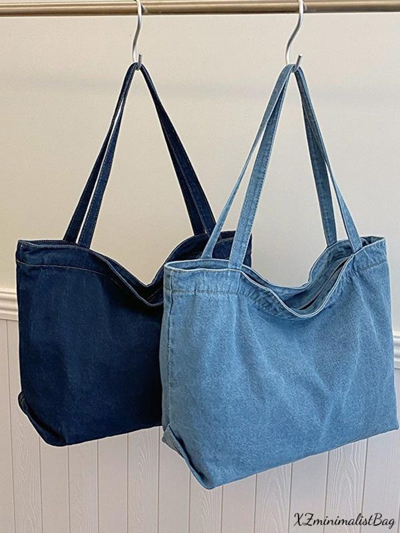 May include: Two denim tote bags hanging from metal hooks. One bag is a dark indigo color, and the other is a lighter blue wash. Both bags have long, thin straps and a rectangular shape. The text "XZminimalistBag" is visible in the bottom right corner.