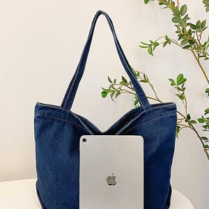 May include: A dark blue denim tote bag with long straps. The bag has a wide opening and is shown with a silver tablet in front. The bag is sitting on a white surface. The text "XZminimalistBag" is at the bottom.